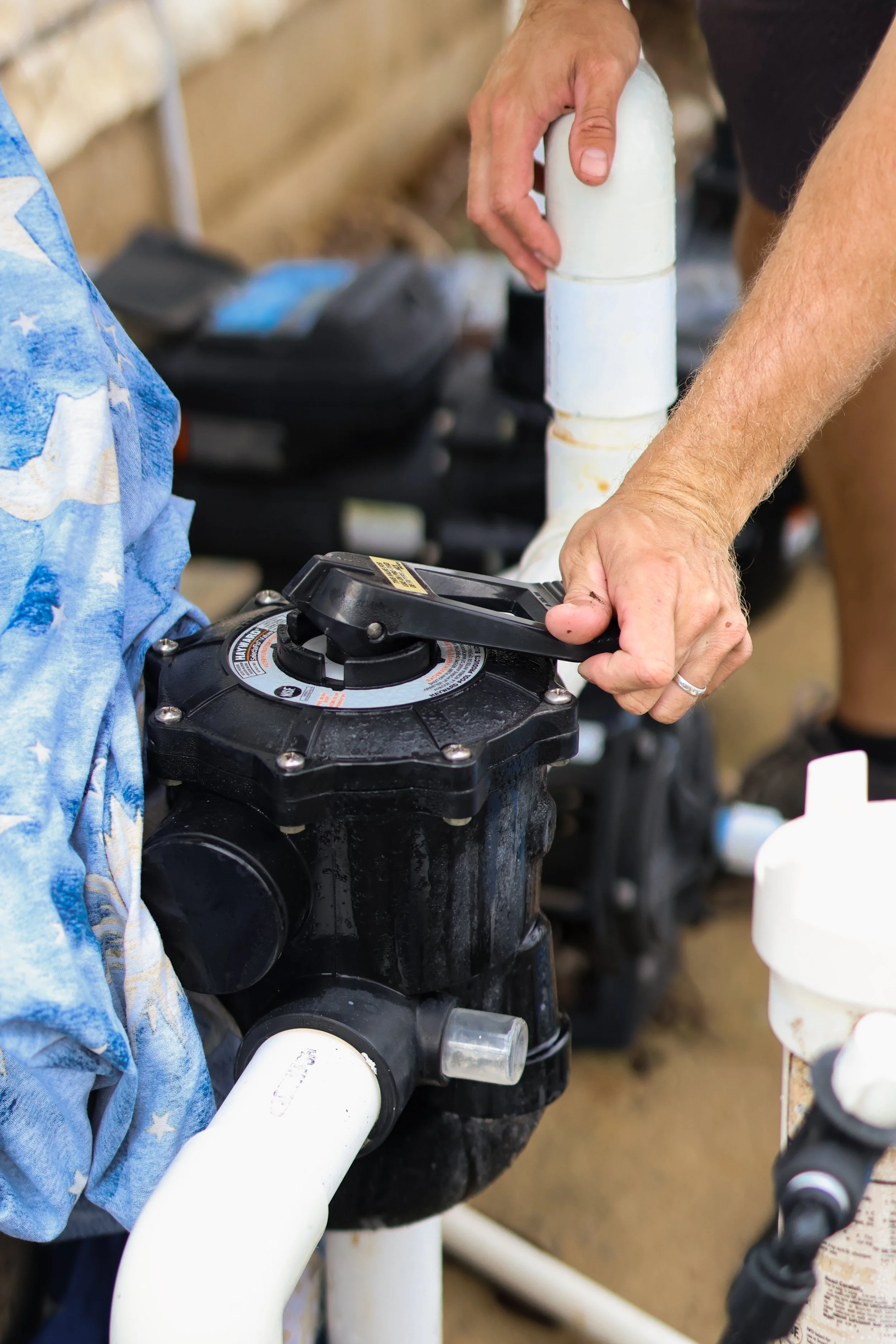 Person adjusting a pool pump valve with white PVC pipes around it.