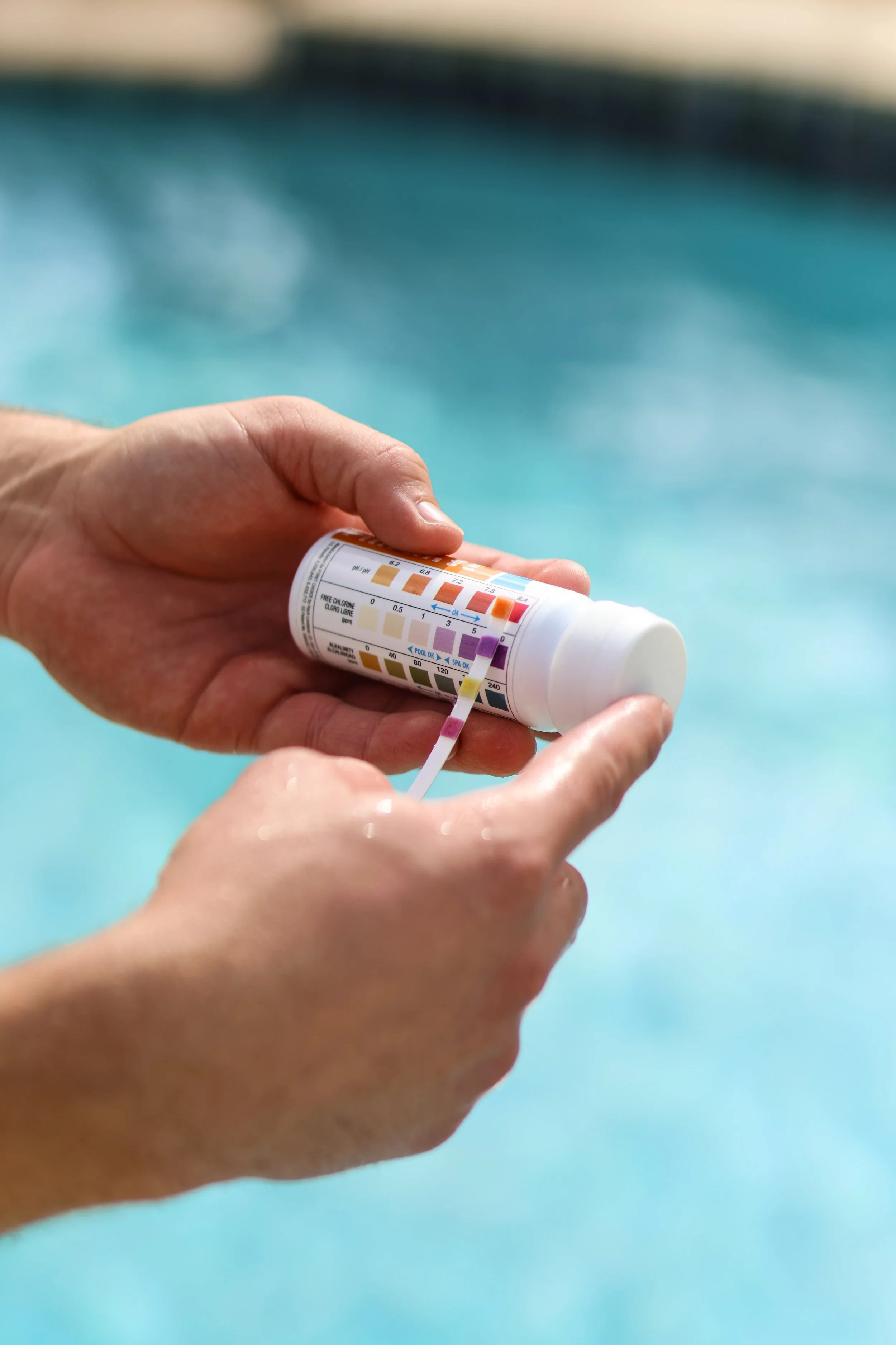 Person holding pool test kit with color chart in front of a swimming pool.